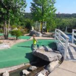 Scenic outdoor miniature golf course at Brookside Miniature Golf in Branson with a child playing near a small bridge and landscaped water feature