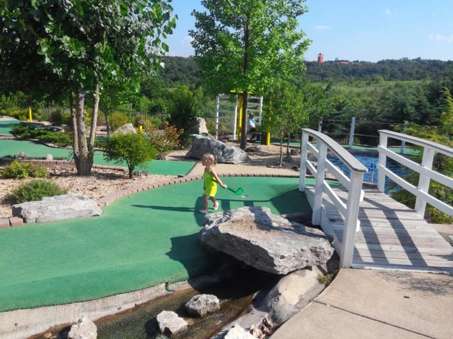 Scenic outdoor miniature golf course at Brookside Miniature Golf in Branson with a child playing near a small bridge and landscaped water feature